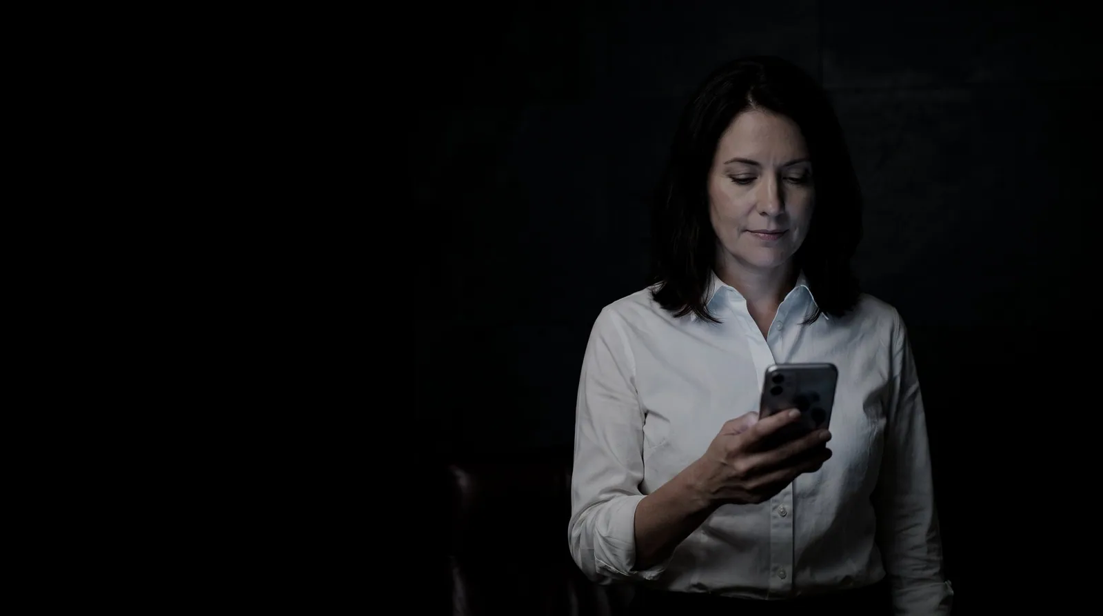 A lawyer reads a message on her phone in a dark office