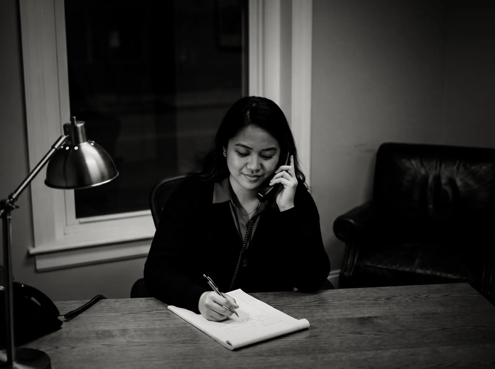 A paralegal answering an evening call at her desk, taking notes on a legal pad